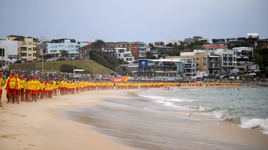 Rettungsschwimmer-fassen-sich-an-den-Haenden-waehrend-sie-drei-Schweigeminuten-einlegen-um-den-Opfern-des-Anschlags-am-Bondi-Beach-in-Sydney-zu-gedenken