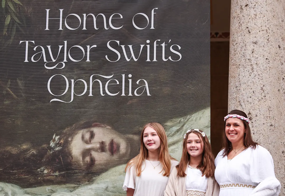 Grace-Poyant-l-r-Emma-Poyant-und-ihre-Mutter-Danielle-Poyant-stehen-als-Ophelia-verkleidet-vor-einem-Banner-mit-der-Aufschrift-Home-of-Taylor-Swifts-Ophelia-Laut-dem-Museum-Wiesbaden-hat-das-Motiv-eine-grosse-Aehnlichkeit-mit-dem-Werk-The-Fate-of-Ophelia-von-Friedrich-Wilhelm-Theodor-Heyser-das-zur-Sammlung-des-Museums-Wiesbaden-gehoert