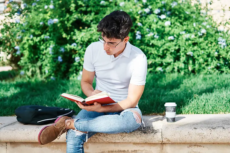 Thoughtful-male-student-reading-book-and-preparing-for-classes-while-sitting-on-stone-border-in-city-in-summer-Model-released-AdalbertoRodriguez-UniversityStudent-2-Copyright-xAdalbertoxRodriguezx