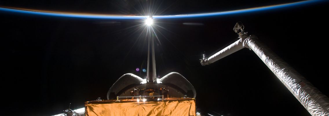 Ein Astronaut hat die Arbeiten im All fotografiert. Im Bildhintergrund ist dünn die Erdatmosphäre zu sehen.