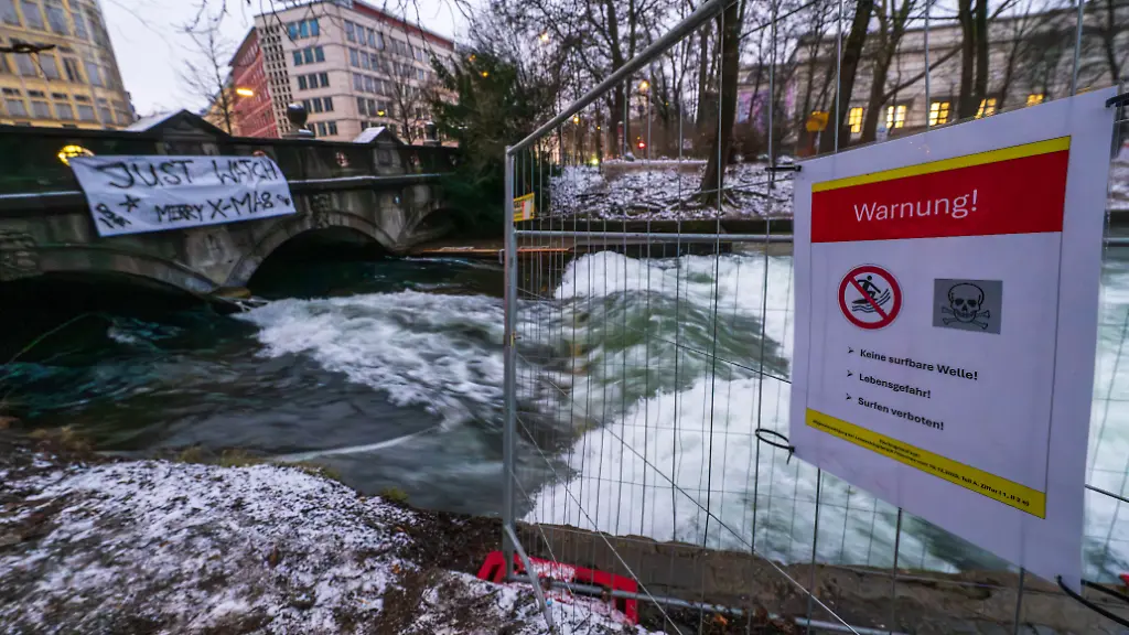 Ein-Schild-mit-der-Aufschrift-Warnung-Keine-surfbare-Welle-Lebensgefahr-Surfen-verboten-ist-an-einem-Zaun-neben-dem-Eisbach-und-der-provisorischen-Eisbachwelle-im-Englischen-Garten-zu-sehen-In-den-vergangenen-zwei-Monaten-hatte-sich-die-Welle-nicht-mehr-aufgebaut-Seit-dem-ersten-Weihnachtstag-koennen-Surfer-wieder-auf-der-stehenden-Welle-reiten-Die-Welle-ist-normalerweise-zu-jeder-Jahres-und-Tageszeit-ein-wahrer-Hotspot-fuer-Touristen-und-Surfer-aus-der-ganzen-Welt