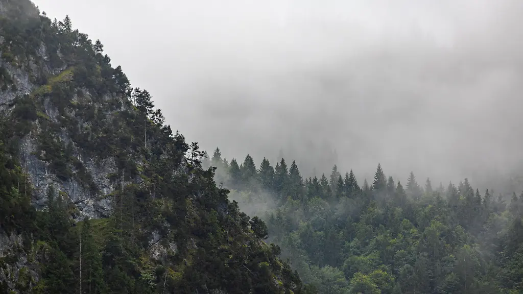 Regenwolken-und-dichter-Nebel-verhuellen-die-Haenge-des-Kofel-Die-markante-Felsformation-in-den-Ammergauer-Alpen-zeigt-sich-an-diesem-Tag-in-mystischer-und-duesterer-Stimmung