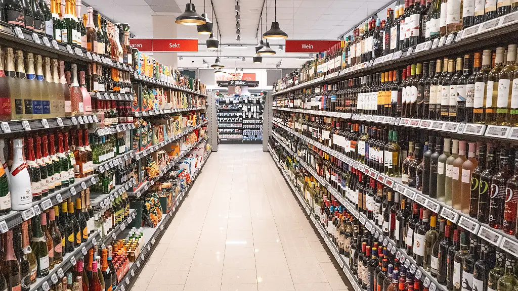 Ein-gut-sortierter-Gang-im-Supermarkt-mit-voll-bestueckten-Regalen-links-und-rechts-Links-verschiedene-Sorten-Sekt-Schaumweine-und-alkoholfreie-Alternativen-daneben-Chips-und-Knabberartikel-Rechts-zahlreiche-Rot-und-Weissweine-sowie-Spirituosen-Die-Szene-zeigt-die-Produktvielfalt-im-Lebensmittelhandel-und-typische-Praesentation-alkoholischer-und-alkoholfreier-Getraenke-Aufgenommen-in-Altshausen-Eibner-Pressefoto-Eky-Eibner