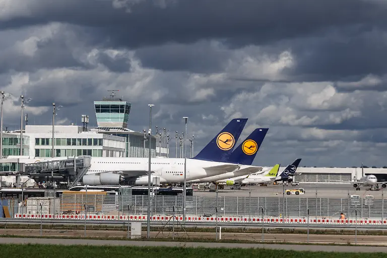 Allgemeine-Ansicht-vom-Flughafen-Muenchen-Bayern-Deutschland-Auf-dem-Vorfeld-vom-Verkehrsflughafen-stehen-zwei-Flugzeuge-der-Fluggesellschaft-Lufthansa-an-der-Fluggastbruecke-am-Gate-In-der-Bildmitte-ist-der-Tower-vom-Satellit-Terminal-2-auf-dem-Flughafengelaende-zu-sehen-Der-Flughafen-Muenchen-Franz-Josef-Strauss-MUC-wird-von-der-Flughafen-Muenchen-GmbH-betrieben