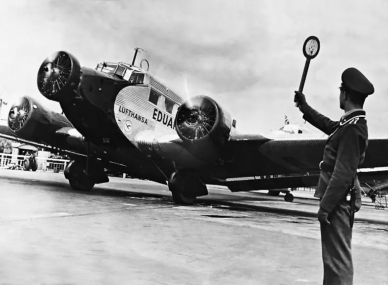 Ein-Bediensteter-der-Luftaufsicht-des-Flughafens-Tempelhof-gibt-dem-Piloten-einer-Junkers-Ju-52-der-Lufthansa-das-Startzeichen