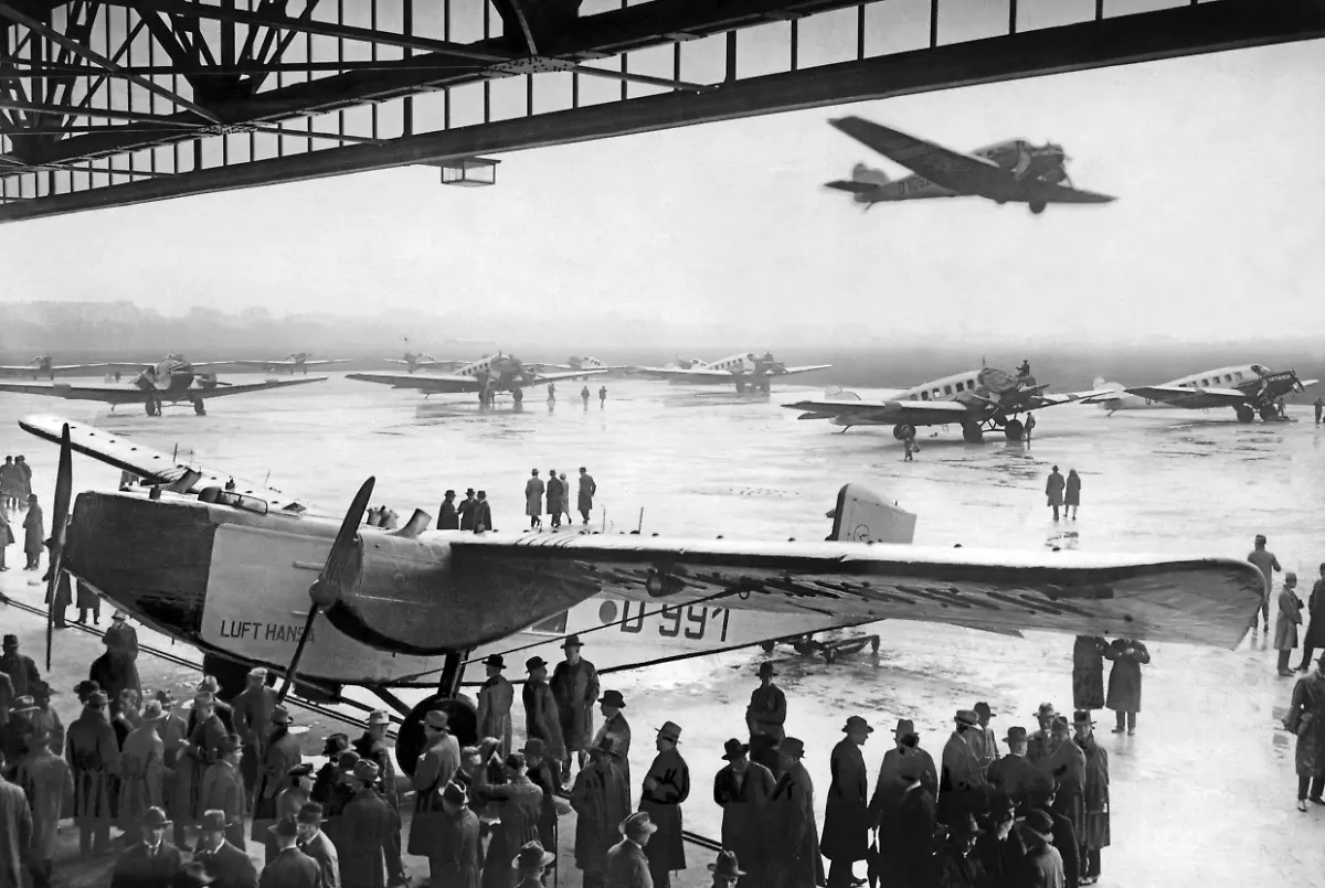 Eroeffnung-des-Sommerflugverkehrs-der-Deutschen-Lufthansa-Auf-dem-Vorfeld-des-Flughafens-Tempelhof-stehen-diverse-Junkers-Flugzeuge-im-Hangar-eine-Rohrbach-Ro-VIII-Roland-Aufnahmedatum-01-01-1927-31-12