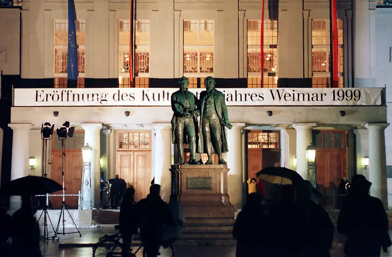 Passanten-stehen-am-19-2-1999-vor-dem-hell-erleuchteten-Deutschen-Nationaltheater-in-der-europaeischen-Kulturhauptstadt-Weimar-im-Vordergrund-das-Goethe-Schiller-Denkmal-Hier-wurde-am-Abend-das-Kulturstadtjahr-1999-offiziell-eroeffnet-Die-thueringische-Klassikerstadt-ist-die-erste-europaeische-Kulturstadt-aus-dem-ehemaligen-Ostblock-Mit-60000-Einwohnern-ist-sie-zugleich-die-bisher-kleinste-Vorgaengerin-war-im-vergangenen-Jahr-die-schwedische-Hauptstadt-Stockholm