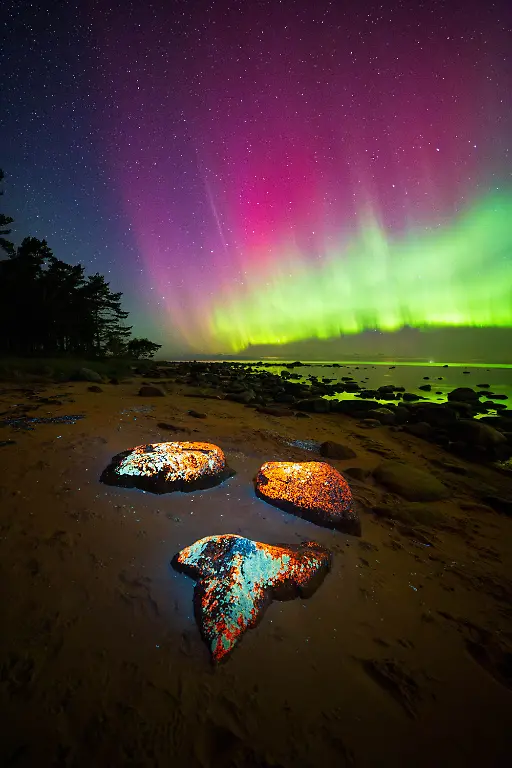 I-shot-this-image-on-a-quiet-rocky-beach-as-a-strong-aurora-storm-rolled-in-from-the-north-At-first-it-was-just-a-low-green-arc-but-it-quickly-erupted-into-vertical-curtains-of-lime-and-rare-magenta-To-connect-the-sky-with-the-foreground-I-illuminated-the-shoreline-rocks-with-a-strong-365-nm-UV-light-torch-which-made-the-minerals-pop-and-added-the-surreal-glow-you-see-in-the-image-The-challenge-was-balancing-everything-an-exposure-of-about-5-seconds-to-keep-the-aurora-structure-sharp-and-managing-the-UV-spill-so-it-didn-t-look-artificial-What-keeps-me-coming-back-to-Northern-Lights-photography-is-this-mix-of-science-and-magic-you-study-forecasts-and-KP-indices-but-the-real-reward-is-when-the-sky-does-something-unexpected-and-you-re-prepared-to-capture-it-in-a-single-colorful-frame