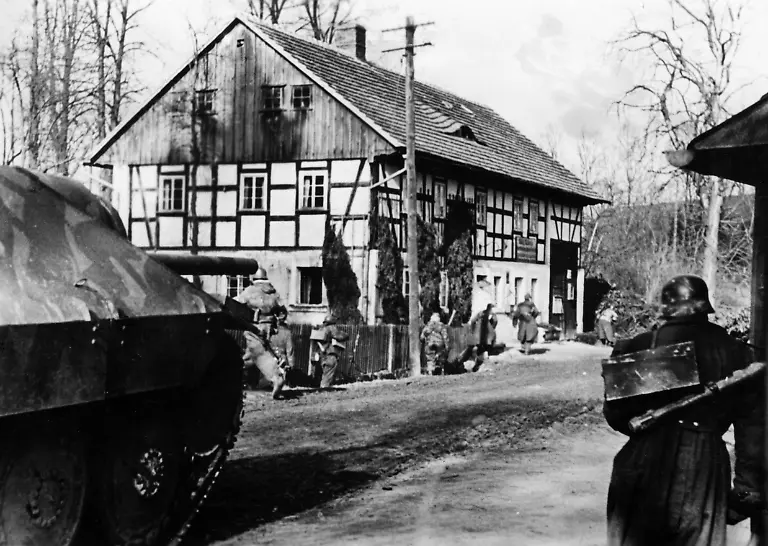 Deutsche-Infanterie-rueckt-unterstuetzt-durch-einen-Jagdpanzer-38-t-Hetzer-in-ein-schlesisches-Dorf-ein-Bei-dem-Soldaten-rechts-im-Bild-handelt-es-sich-um-den-2-Schuetzen-einer-Mg-Mannschaft-welcher-Munition-und-weitere-Laeufe-fuer-die-Waffe-am-Ruecken-traegt