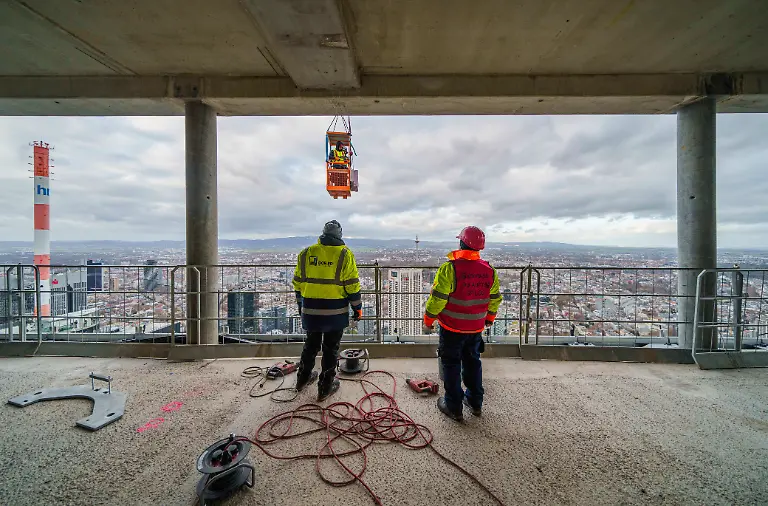 Im-52-Stock-sind-zwei-Maenner-in-einer-Gondel-mit-Arbeiten-an-der-Aussenfassade-beschaeftigt-FOUR-ist-der-Name-fuer-das-Bauprojekt-auf-dem-als-Deutsche-Bank-Dreieck-bekannte-Areal-des-Projektentwicklers-Gross-Partner-Grundstuecksentwicklungsgesellschaft-Die-Rohbauten-der-vier-Hochhaustuerme-sind-fast-abgeschlossen-Fertigstellung-fuer-2025-geplant