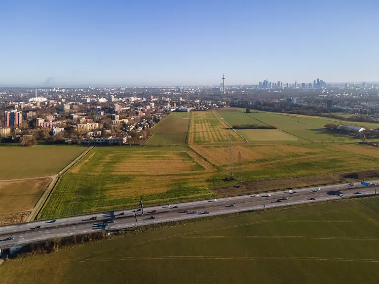 Die-Felder-im-Nordwesten-von-Frankfurt-am-Main-sind-gelb-gruen-bewachsen-Luftaufnahme-mit-einer-Drohne-Auf-diesem-etwa-550-Hektar-umfassenden-Gebiet-zwischen-Praunheim-der-Nordweststadt-Niederursel-sowie-den-Nachbargemeinden-Steinbach-und-Weisskirchen-soll-entlang-der-Bundesautobahn-A5-der-neue-Stadtteil-der-Quartiere-mit-6-800-Wohnungen-fuer-17-000-Menschen-sowie-5-000-neuen-Arbeitsplaetzen-entstehen-Das-Projekt-soll-etwa-1-Milliarde-Euro-kosten