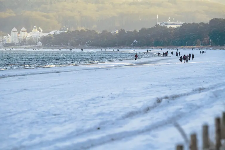 Spaziergaenger-sind-am-verschneiten-Ostseestrand-unterwegs-Eis-und-Schnee-haben-den-Norden-fest-im-Griff