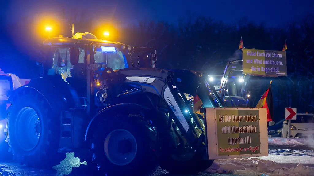 Traktoren-blockieren-am-fruehen-Morgen-auf-der-Autobahn-A-24-die-Autobahnabfahrt-Kremmen-Auf-den-Schildern-steht-Ist-der-Bauer-ruiniert-wird-klimaschaedlich-importiert-und-Huetet-Euch-vor-Sturm-und-Wind-und-Bauern-die-in-Rage-sind-Der-Bauernbund-Brandenburg-protestiert-damit-gegen-das-Mercosur-Freihandelsabkommen