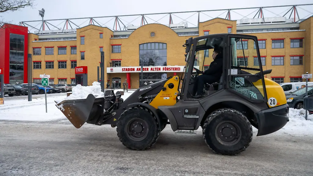 Fussball-Herren-Saison-2025-2026-1-Bundesliga-1-FC-Union-Berlin-freiwillige-Fans-und-Angestellte-befreien-Wege-und-Parkplaetze-am-und-im-Stadion-An-der-Alten-Foersterei-von-Schnee-im-Bild-ein-Stadionmitarbeiter-bringt-mit-einem-Bagger-Schnee-weg-08-01