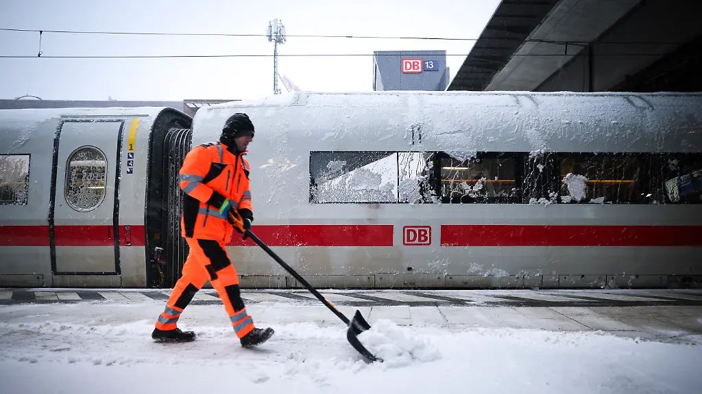 Ein-Mitarbeiter-schiebt-Schnee-von-einem-Bahnsteig-am-Hauptbahnhof-an-dem-ein-abgestellter-ICE-steht-Die-Deutsche-Bahn-hat-wegen-des-stuermischen-Winterwetters-den-Fernverkehr-im-Norden-Deutschlands-bis-mindestens-zum-Mittag-eingestellt