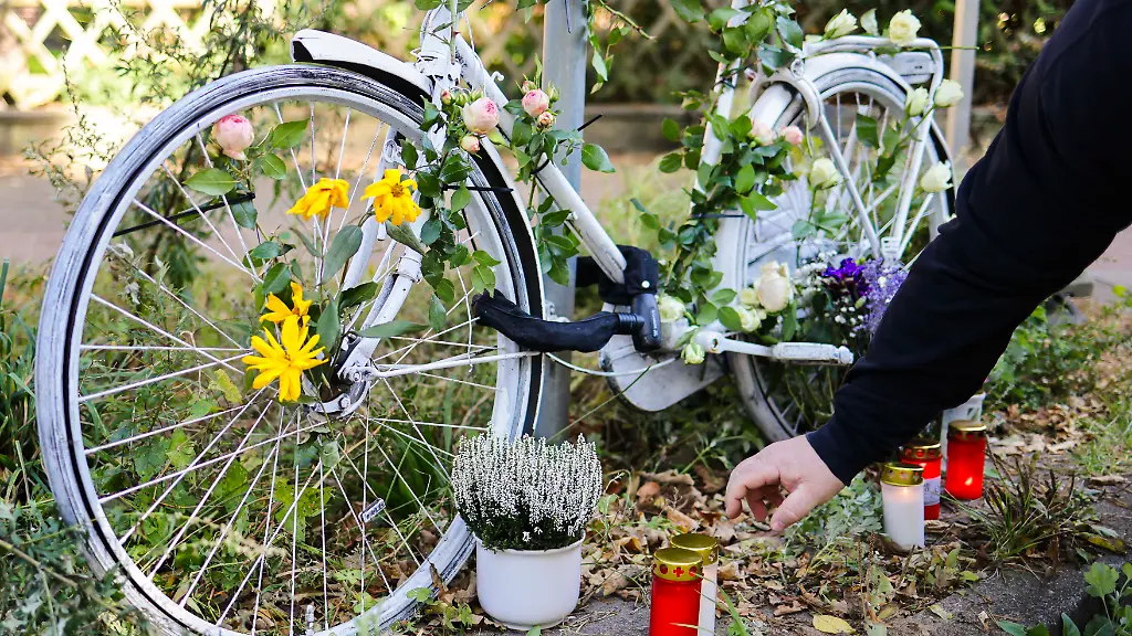 Ein-Teilnehmer-einer-Mahnwache-stellt-eine-Kerze-neben-ein-weiss-lackiertes-Ghostbike-im-Bahrenfelder-Kirchenweg-Hier-hat-der-Allgemeine-Deutsche-Fahrrad-Club-einem-Fahrradfahrer-gedacht-der-am-17-September-2025-in-Hamburg-Altona-toedlich-verletzt-wurde-Ein-Autofahrer-hatte-nach-dem-Parken-die-Autotuer-geoeffnet-und-dem-Fahrradfahrer-dabei-vom-Rad-gestossen