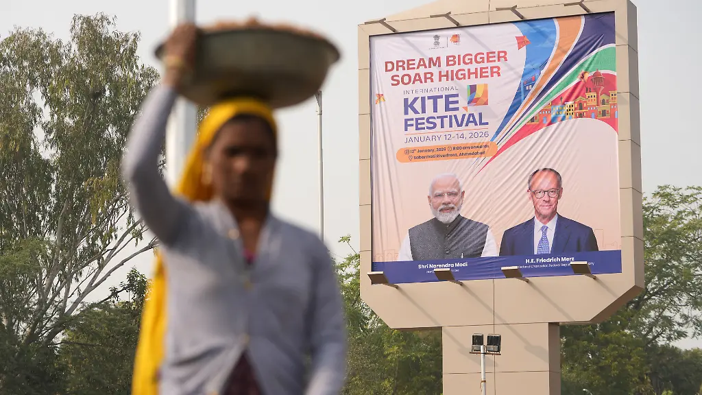 Eine-Frau-geht-an-einem-Plakat-des-indischen-Premierministers-Narendra-Modi-l-und-des-deutschen-Bundeskanzlers-Friedrich-Merz-CDU-vor-ihrem-Besuch-in-Ahmedabad-vorueber-Bundeskanzler-Merz-reist-vom-11-13-Januar-2026-nach-Indien