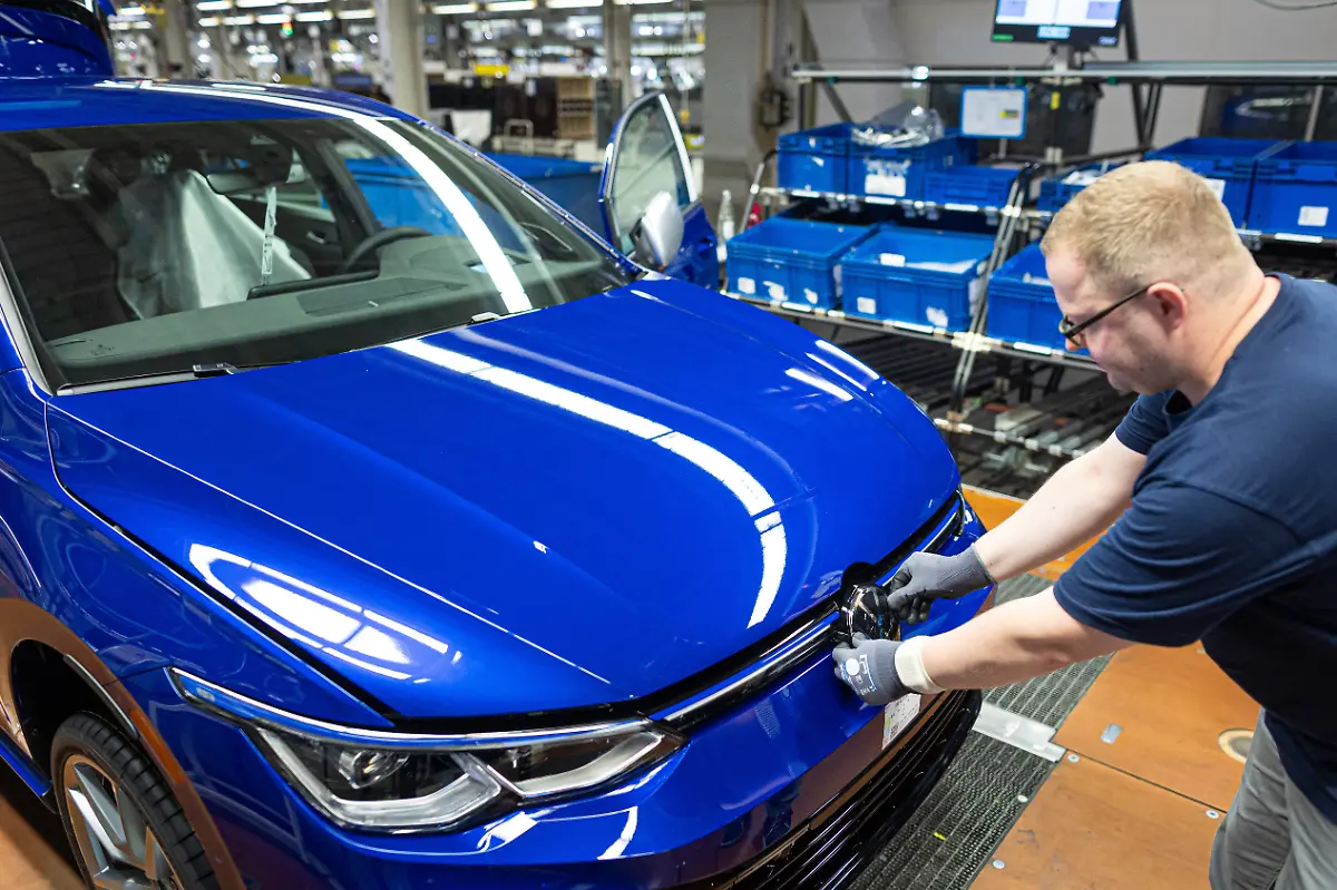 Ein-Mitarbeiter-bringt-bei-einem-Volkswagen-Golf-im-VW-Werk-in-der-Endmontage-das-Logo-an