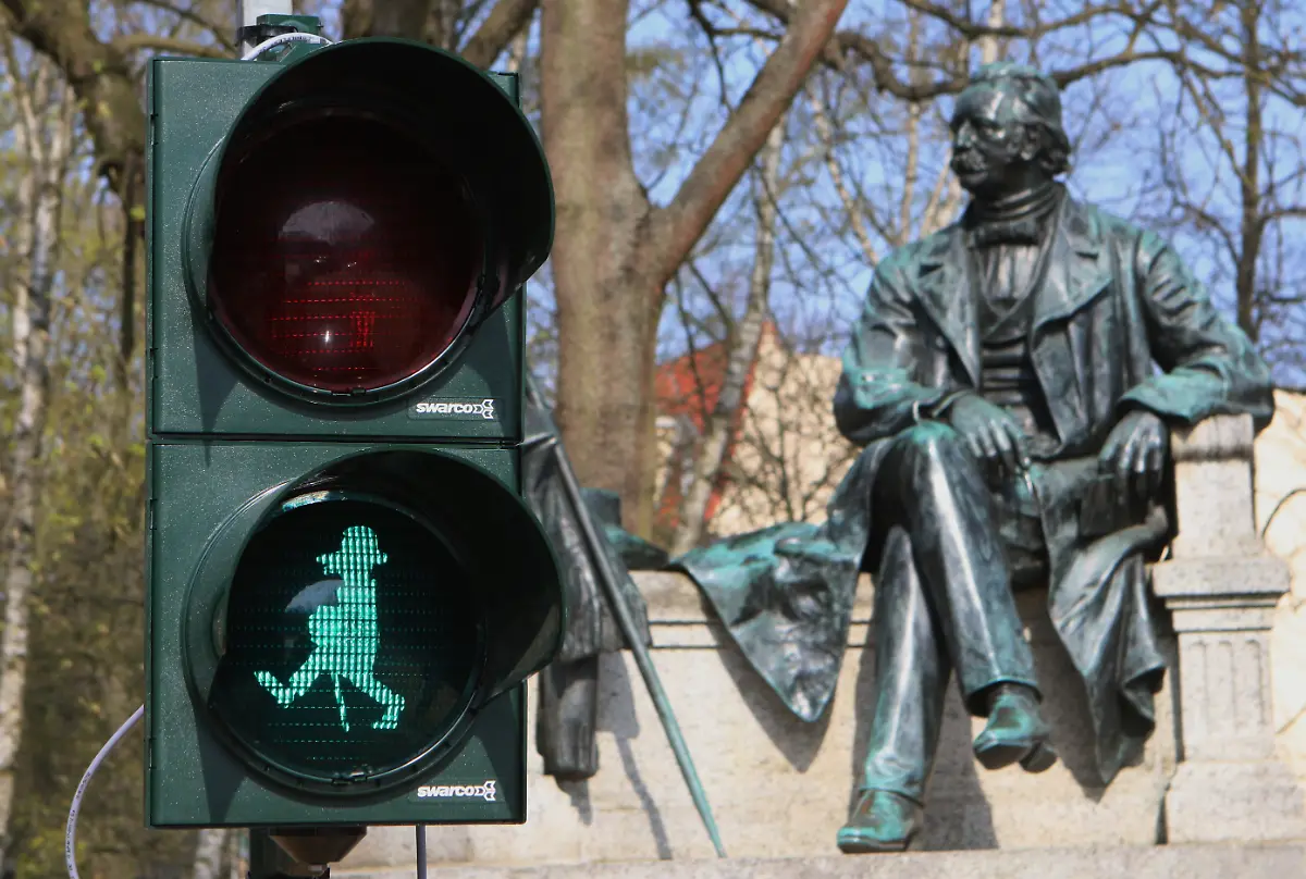 Vor-dem-Fontane-Denkmal-am-Fontaneplatz-steht-eine-Fussgaengerampel-mit-einem-Abbild-des-Schriftstellers-Theodor-Fontane-als-Ampelmaennchen-Die-Ampel-wurde-im-Rahmen-des-Fontane-Jahres-in-Betrieb-genommen-Die-roten-und-gruenen-Ampelbilder-sind-Sonderanfertigungen-die-der-Kuenstler-Max-Otto-Stoye-im-Auftrag-der-Stadt-entwarf-Sie-zeigen-Fontane-als-Silhouette-einmal-gehend-mit-Hut-und-Stock-und-einmal-stehend-mit-Hut-in-der-Hand