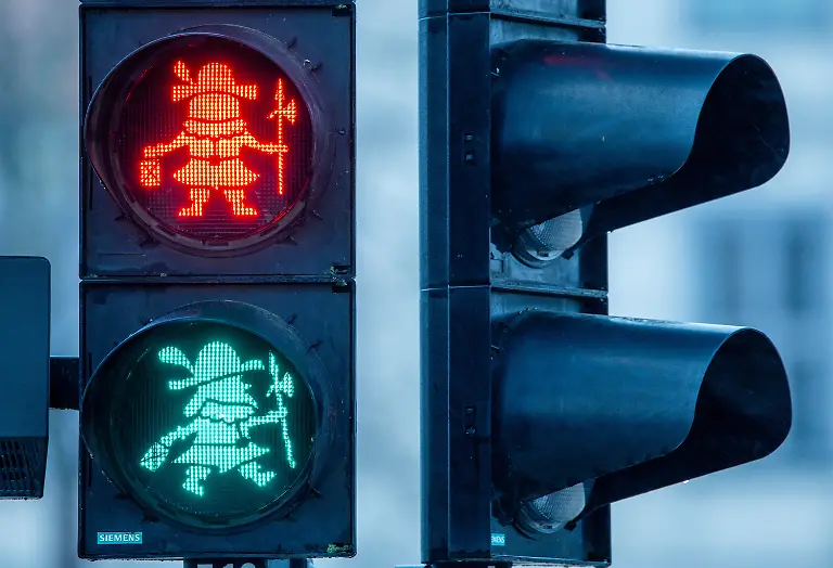 In-der-Fussgaengerampel-vor-dem-Schweriner-Schloss-leuchtet-der-Schlossgeist-Petermaennchen-in-rot-und-gruen-auf-Seit-einem-Jahr-hat-die-Sagengestalt-das-normale-Ampelmaennchen-abgeloest-Im-Jahr-2017-gab-es-zu-diesem-Thema-eine-grosse-politische-Debatte-in-der-Stadtverwaltung-Nach-sechs-Jahren-und-vielen-behoerdlichen-Bearbeitungsstufen-konnte-Petermaennchen-im-April-2023-seinen-Dienst-vor-dem-Schloss-antreten