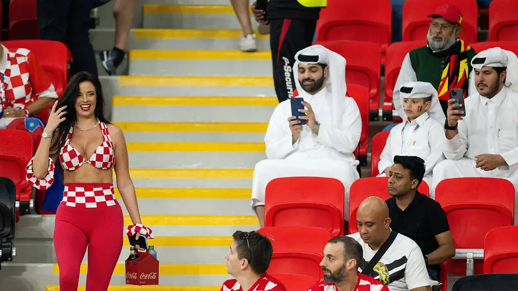 IMAGO-Iconic-Moments-Fussball-Bilder-des-Jahres-Sport-12-Dezember-Sport-Themen-der-Woche-KW48-Sport-Bilder-des-Tages-221201-Croatian-model-Ivana-Knoll-walks-past-men-in-traditional-Qatari-clothing-during-the-FIFA-World-Cup-WM-Weltmeisterschaft-Fussball-2022-football-match-between-Croatia-and-Belgium-on-December-1-2022-in-Doha-Knoll-s-way-of-dressing-has-challenged-the-laws-of-Qatar-where-the-rules-for-women-are-quite-strict