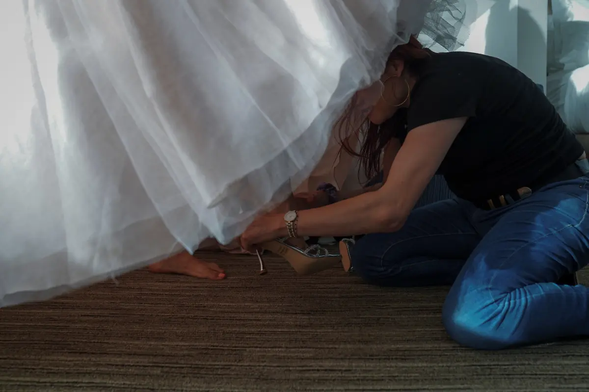 Stephanie-Summers-36-helps-Jessica-Flores-49-put-on-her-shoes-as-she-gets-ready-for-her-quinceanera-at-a-hotel-in-Houston-Texas-U-S-May-14-2025-Flores-and-other-transgender-Latina-immigrants-were-recently-able-to-celebrate-this-year-as-quinceaneras-literally-translated-as-15-year-olds-thanks-to-the-Organizacion-Latina-de-Trans-en-Texas-a-group-promoting-rights-for-LGBTQ-people-including-transgender-women-from-Latin-America-I-am-very-excited-I-still-have-that-feeling-from-when-I-was-a-little-girl-that-it-s-going-to-come-true-today-said-Flores-Truly-I-feel-that-excitement-as-if-I-were-fifteen-years-old-REUTERS-Gabriel-V-Cardenas-SEARCH-CARDENAS-U-S-QUINCEANERAS-FOR-THIS-STORY-SEARCH-WIDER-IMAGE-FOR-ALL-STORIES-THIS-IMAGE-IS-ONLY-FOR-USE-WITH-THE-STORY-USA-LGBTQ-QUINCEANERAS-NO-STANDALONE-USES