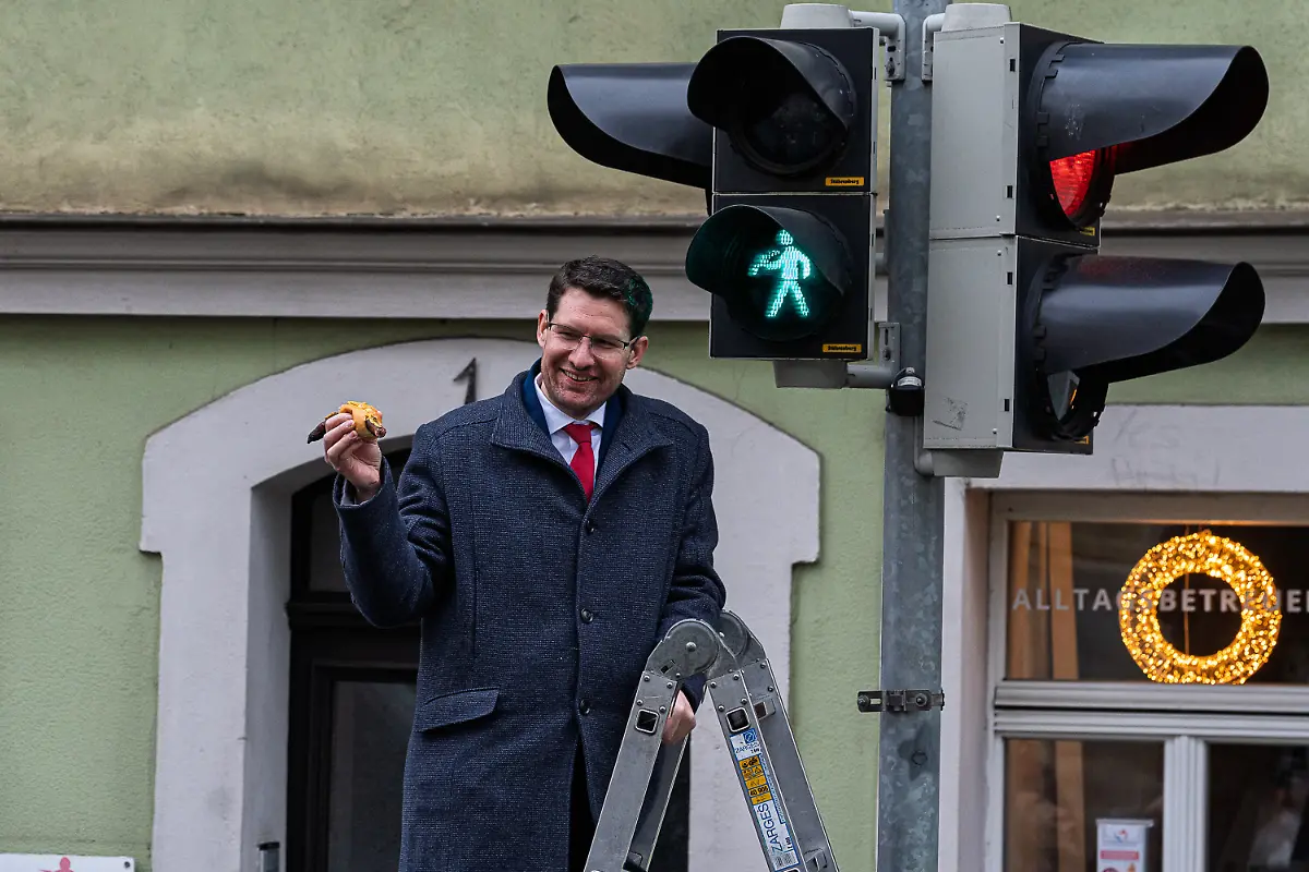Coburgs-Oberbuergermeister-Dominik-Sauerteig-SPD-stellt-das-neue-Ampelmaennchen-vor-das-eine-Bratwurst-im-Semmel-in-der-Hand-haelt-Die-Bratwurst-ist-wahrscheinlich-fuer-viele-Menschen-das-Typischste-fuer-Franken-die-Coburger-wuerdigen-die-beliebte-Speise-nun-auf-ihre-Weise-mit-einem-eigenen-Ampelmaennchen-zu-dpa-Bei-der-Bratwurst-versteht-der-Coburger-viel-Spass