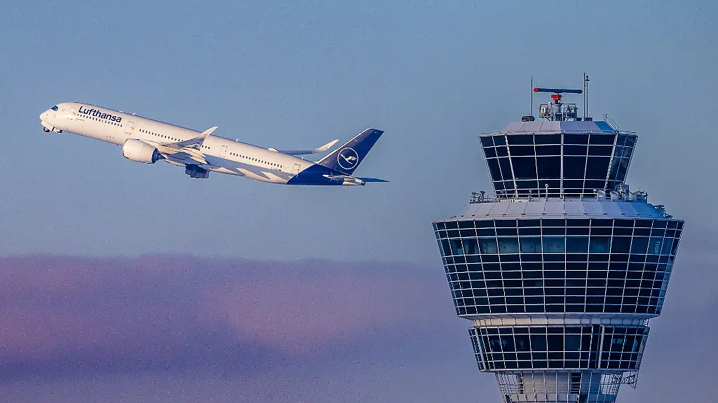 Ein-Airbus-A350-der-Lufthansa-befindet-sich-im-Steigflug-bei-winterlichem-Wetter-nahe-dem-Tower-des-Flughafens-Muenchen-Der-Kontrollturm-ist-rechts-im-Bild-deutlich-sichtbar-waehrend-das-Passagierflugzeug-im-Hintergrund-vor-Abendwolken-aufsteigt-Flughafen-Muenchen-im-Schneebetrieb-waehrend-Kaeltewelle-in-Bayern-Oberding-11-01