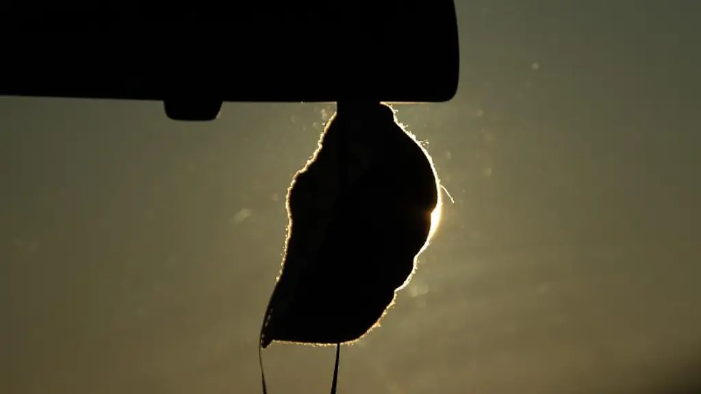 Eine-FFP2-Maske-haengt-vor-der-aufgehenden-Sonne-in-einem-Auto