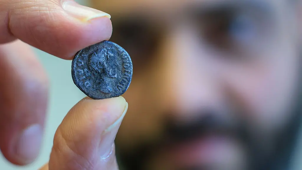 Ein-Mitarbeiter-des-Landesamtes-fuer-Denkmalpflege-und-Archaeologie-praesentiert-eine-roemische-Muenze-aus-dem-fruehen-3-Jahrhundert-nach-Christus