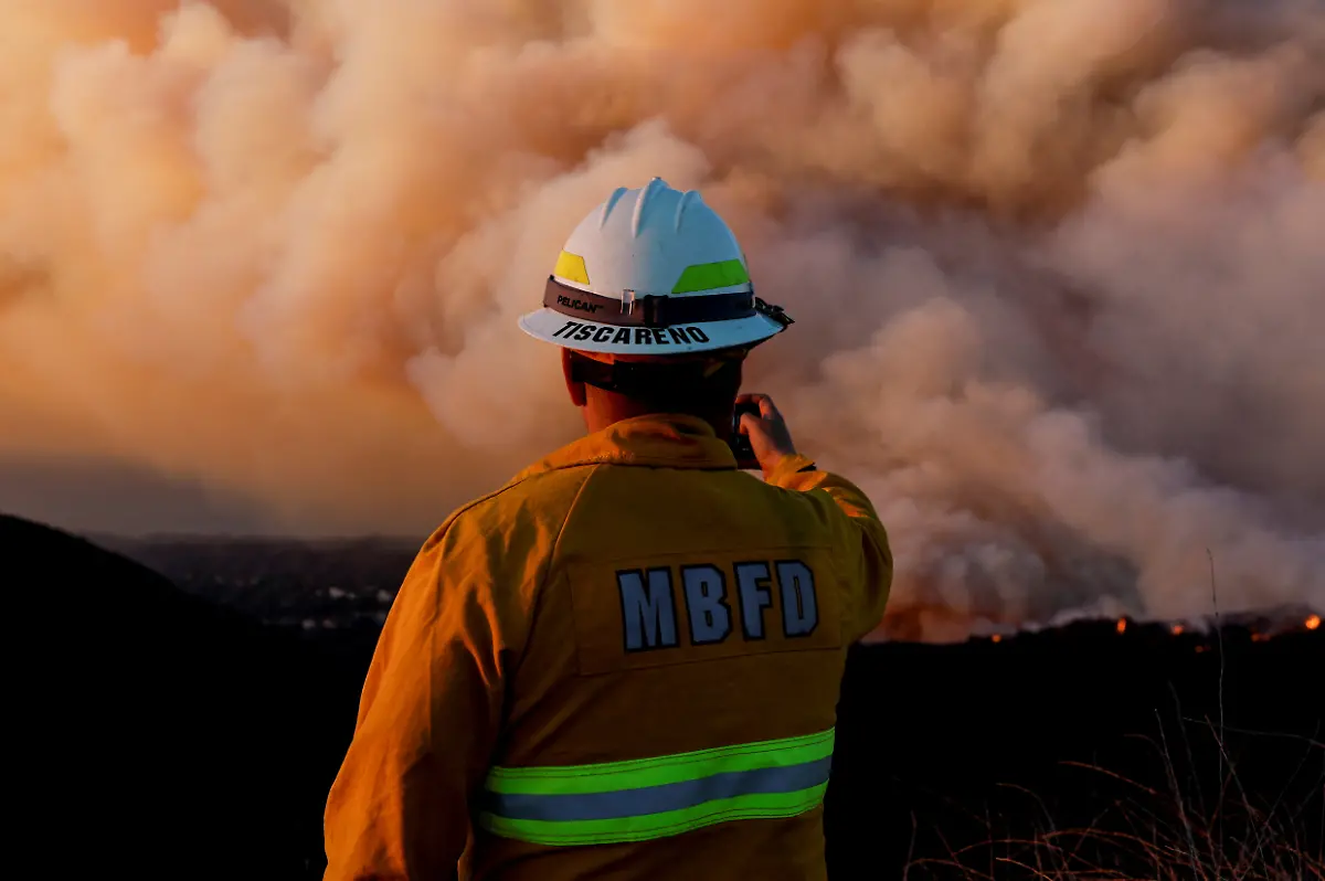 A-member-of-the-Manhattan-Beach-Fire-Department-holds-a-smartphone-as-smoke-billows-from-the-Palisades-Fire-threatening-homes-in-the-Brentwood-area-of-Los-Angeles-California-U-S-January-11-2025
