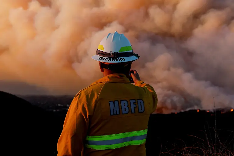 A-member-of-the-Manhattan-Beach-Fire-Department-holds-a-smartphone-as-smoke-billows-from-the-Palisades-Fire-threatening-homes-in-the-Brentwood-area-of-Los-Angeles-California-U-S-January-11-2025