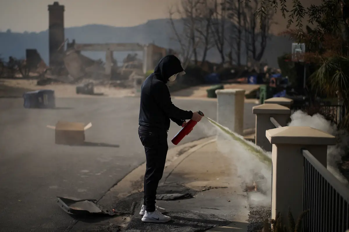 A-resident-tries-to-extinguish-a-smouldering-fire-on-his-house-after-powerful-winds-fueling-devastating-wildfires-in-the-Los-Angeles-area-forced-people-to-evacuate-in-the-Palisades-Highlands-neighborhood-on-the-west-side-of-Los-Angeles-California-U-S-January-9-2025