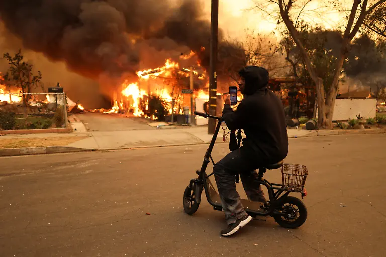 A-person-uses-a-cellphone-in-front-of-a-burning-house-as-powerful-winds-fueling-devastating-wildfires-in-the-Los-Angeles-area-force-people-to-evacuate-at-the-Eaton-Fire-in-Altadena-California-U-S-January-8-2025