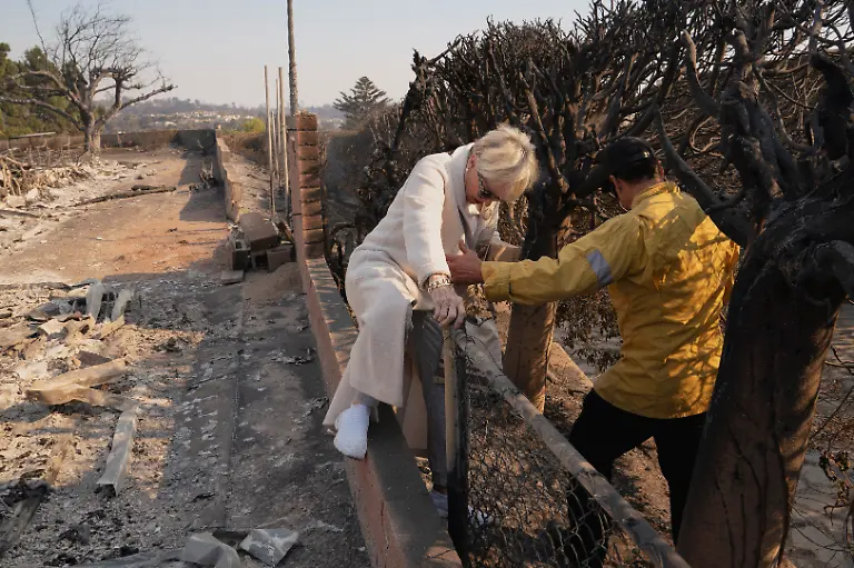 Holly-Richter-accesses-her-home-which-was-spared-from-the-Palisades-Fire-with-the-help-of-a-firefighter-by-walking-through-the-yard-of-her-neighbor-s-destroyed-home-in-the-Pacific-Palisades-neighborhood-in-Los-Angeles-California-U-S-January-10-2025