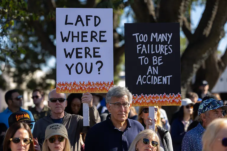 Demonstrators-hold-signs-questioning-the-response-to-the-Palisades-fire-during-a-rally-marking-the-first-anniversary-of-the-deadly-wildfire-in-the-Pacific-Palisades-neighborhood-of-Los-Angeles-on-Jan-7-2026