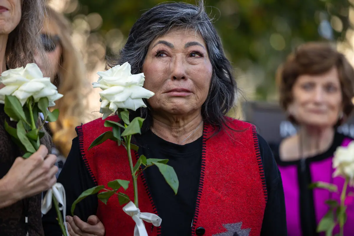 A-woman-holds-a-white-rose-during-a-rally-marking-the-first-anniversary-of-the-deadly-Palisades-fire-in-the-Pacific-Palisades-neighborhood-of-Los-Angeles-on-Jan-7-2026-Residents-gathered-to-honor-the-victims-and-call-for-fairness-accountability-and-a-commitment-to-rebuilding-after-the-wildfire-that-killed-12-people-and-displaced-thousands
