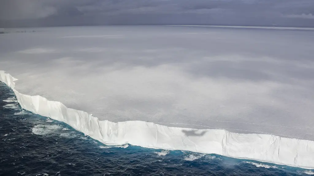 An-iceberg-that-has-survived-for-40-years-for-many-as-the-worlds-largest-is-finally-coming-to-a-slushy-end-Iceberg-A-23A-which-first-broke-away-from-Antarcticas-Filchner-Ice-Shelf-in-1986-is-nearing-the-end-of-its-unusually-long-life-after-nearly-40-years-drifting-through-the-Southern-Ocean-Once-almost-4-000-km-nearly-twice-the-size-of-Rhode-Island-it-has-shrunk-to-about-1-182-km-by-early-January-2026-due-to-repeated-breakups-during-2025-Recent-satellite-and-astronaut-imagery-from-late-December-2025-show-the-iceberg-covered-in-extensive-blue-meltwater-ponds-a-sign-of-advanced-structural-weakening-Scientists-explain-that-pooled-water-forces-cracks-open-accelerating-disintegration-A-thin-white-rim-around-the-berg-marks-a-rampart-moat-effect-where-melting-edges-cause-the-ice-to-flex-upward-and-trap-water-on-top-Linear-blue-and-white-patterns-visible-on-the-surface-are-ancient-glacial-striations-formed-hundreds-of-years-ago-when-the-ice-scraped-across-Antarctic-bedrock-These-subtle-ridges-now-channel-meltwater-across-the-iceberg-Researchers-also-detected-signs-of-a-blowout-where-pressurised-meltwater-punched-through-the-icebergs-edge-spilling-freshwater-into-the-ocean-below-With-A-23A-now-drifting-in-relatively-warm-3-C-waters-scientists-expect-it-to-fully-disintegrate-within-days-or-weeks-A-23As-journey-has-been-exceptional-grounded-in-the-Weddell-Sea-for-over-30-years-freed-in-2020-it-was-trapped-temporarily-in-a-rotating-Taylor-column-before-nearly-colliding-with-South-Georgia-Island-and-then-finally-breaking-apart-rapidly-in-open-ocean-Featuring-A-23A-photographed-from-an-RAF-Atlas-A400M-aircraft-in-January-2025-Where-South-Georgia-Antarctica-When-13-Jan-2026-Credit-UK-MOD-Crown-copyright-Cover-Images-EDITORIAL-USE-ONLY-MATERIALS-ONLY-TO-BE-USED-IN-CONJUNCTION-WITH-EDITORIAL-STORY