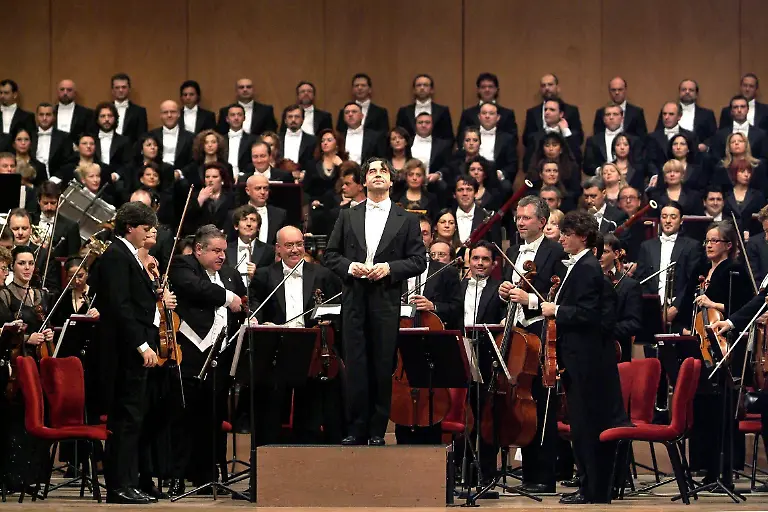 Stardirigent-Riccardo-Muti-steht-mit-den-Musikern-zu-Beginn-des-Festkonzerts-am-14-12-2003-in-der-La-Fenice-in-Venedig-auf-der-Buehne-Fast-acht-Jahre-nach-seiner-Zerstoerung-durch-einen-verheerenden-Brand-ist-das-Opernhaus-mit-einem-umjubelten-Festkonzert-wiedereroeffnet-worden-Auf-dem-Programm-des-von-Muti-geleiteten-Abends-standen-Werke-von-Beethoven-Strawinsky-Caldara-und-Wagner-Das-Publikum-spendete-Muti-und-dem-Orchester-lang-anhaltenden-Applaus-Am-29-Januar-1996-war-die-Fenice-zu-deutsch-Phoenix-die-fuer-ihre-einmalige-Akustik-weltbekannt-war-innerhalb-weniger-Stunden-bis-auf-die-Grundmauern-abgebrannt-Die-Fenice-ist-originalgetreu-wieder-aufgebaut-worden