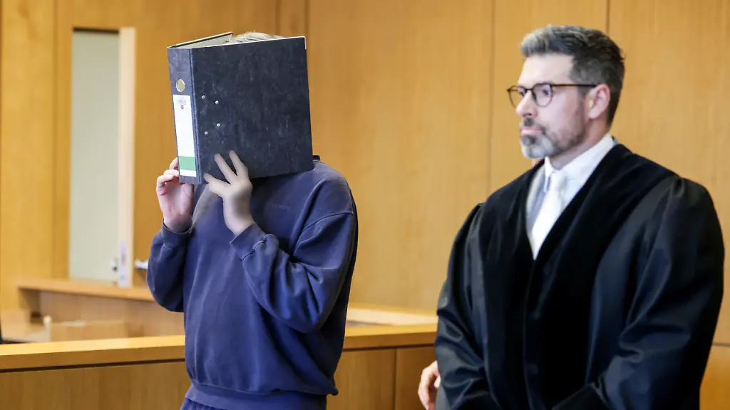 Der-Angeklagte-Krankenpfleger-l-kommt-mit-einem-Aktenordner-vor-dem-Gesicht-in-den-Gerichtssaal-Das-Aachener-Landgericht-hat-einen-Krankenpfleger-wegen-des-Mordes-an-zehn-Patienten-zu-einer-lebenslangen-Freiheitsstrafe-verurteilt