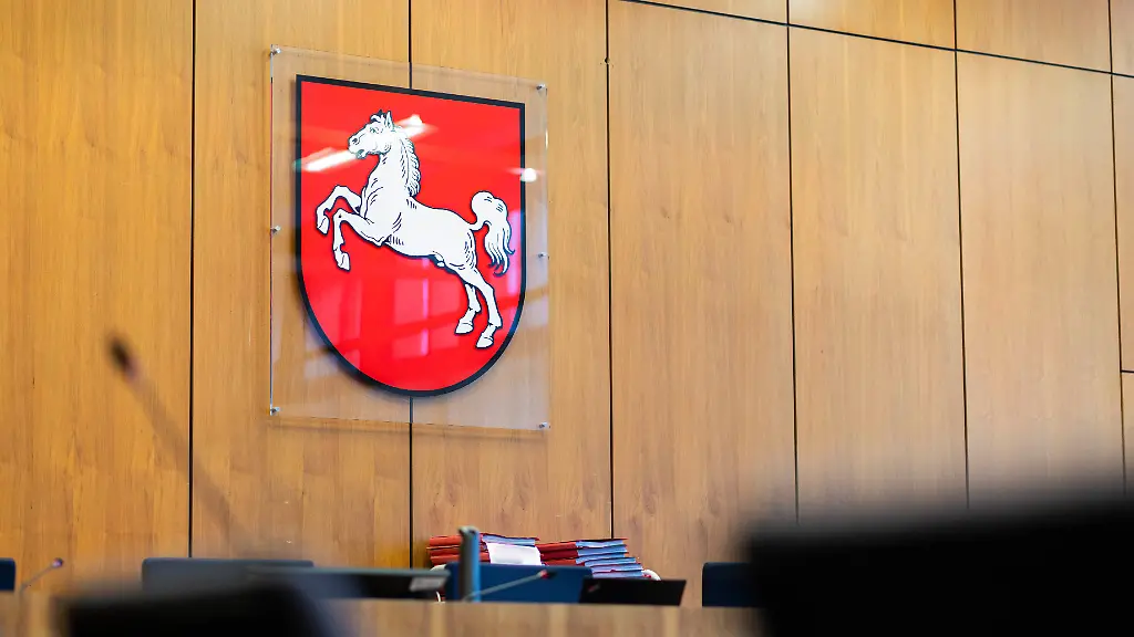 Das-Landeswappen-von-Niedersachsen-haengt-in-einem-Gerichtssaal-im-Justizzentrum-Hildesheim-Ein-Mann-ist-wegen-versuchten-Mordes-und-Totschlags-angeklagt-Er-soll-wiederholt-mit-einem-Brecheisen-auf-den-Kopf-seiner-ehemaligen-Lebensgefaehrtin-eingeschlagen-und-die-Frau-eine-Treppe-hinabgestossen-haben-Die-Frau-starb-am-Tatort-in-Edemissen