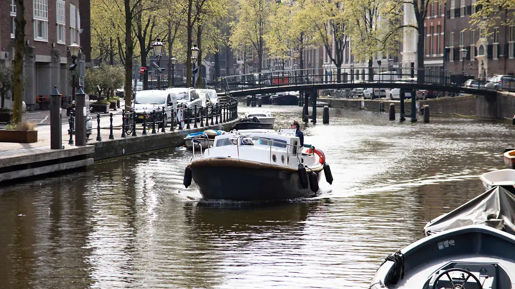 Daily-life-in-the-canals-of-Amsterdam-in-the-Netherlands-with-people-enjoying-drinks-next-to-the-water-or-having-a-boat-tour-The-17th-century-canal-ring-area-known-as-Venice-of-the-North-is-a-UNESCO-World-Heritage-Site-in-the-Dutch-capital-The-scenes-with-the-overcrowded-tourists-didn-t-occur-in-April-as-there-were-travel-restrictions-applied-due-to-Covid-19-Coronavirus-pandemic-Amsterdam-the-Netherlands-on-April-28-2021