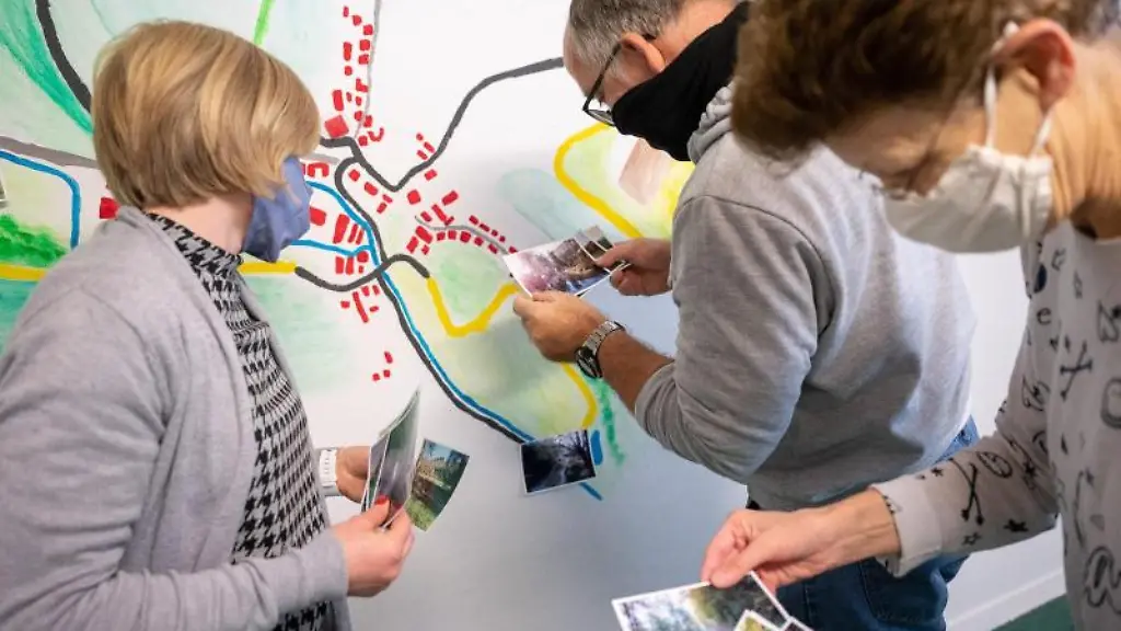 Zwei-Klienten-der-Bruderhaus-Diakonie-r-arbeiten-in-einem-Atelier-mit-einer-Betreuerin-an-einer-Karte