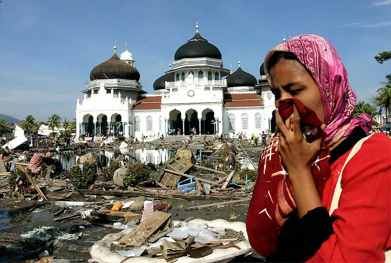 A-woman-walks-near-a-mosque-with-the-rubbish-from-the-quake-and-tsunami-in-Banda-Aceh-Tuesday-Dec-28-2004-The-Health-Ministry-said-in-a-statement-early-Wednesday-that-27-178-people-have-been-killed-on-Indonesia-s-Sumatra-Island