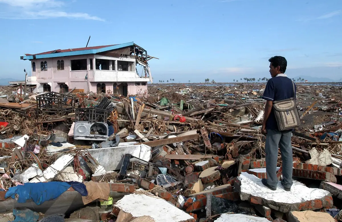 ARCHIV-Alexander-Julkarnaen-39-steht-zwischen-den-Truemmern-seines-Hauses-und-Heimatortes-in-Banda-Aceh-Archivfoto-vom-09-01-2005-Bei-der-furchtbaren-Tsunami-Katastrophe-von-2004-kommen-am-zweiten-Weihnachtstag-mehr-als-230-000-Menschen-ums-Leben-Gewaltige-Flutwellen-verwuesten-innerhalb-weniger-Stunden-die-Kuesten-des-Indischen-Ozeans-Ausloeser-ist-ein-schweres-Erdbeben-der-Staerke-9-1-vor-der-Kueste-der-indonesischen-Insel-Sumatra-Mindestens-1-5-Millionen-Menschen-werden-obdachlos-Foto-EPA-ANDY-RAIN-zu-dpa-Paket-Chronologie-der-Flutkatastrophe-in-Suedasien-2004-vom-16-12