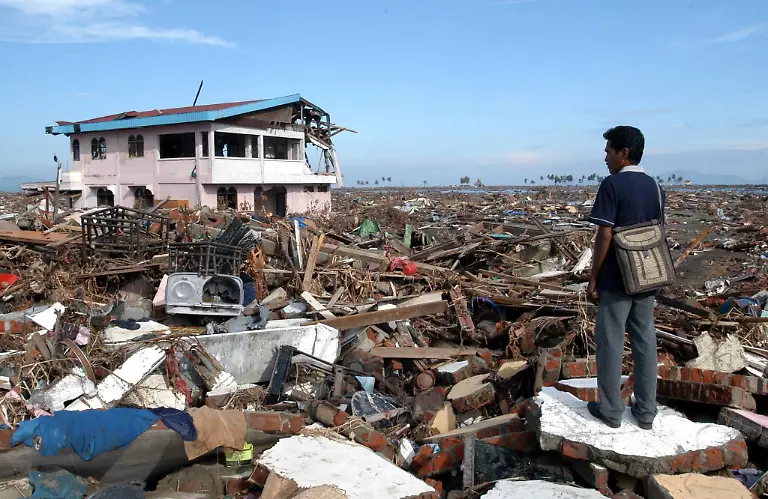 ARCHIV-Alexander-Julkarnaen-39-steht-zwischen-den-Truemmern-seines-Hauses-und-Heimatortes-in-Banda-Aceh-Archivfoto-vom-09-01-2005-Bei-der-furchtbaren-Tsunami-Katastrophe-von-2004-kommen-am-zweiten-Weihnachtstag-mehr-als-230-000-Menschen-ums-Leben-Gewaltige-Flutwellen-verwuesten-innerhalb-weniger-Stunden-die-Kuesten-des-Indischen-Ozeans-Ausloeser-ist-ein-schweres-Erdbeben-der-Staerke-9-1-vor-der-Kueste-der-indonesischen-Insel-Sumatra-Mindestens-1-5-Millionen-Menschen-werden-obdachlos-Foto-EPA-ANDY-RAIN-zu-dpa-Paket-Chronologie-der-Flutkatastrophe-in-Suedasien-2004-vom-16-12