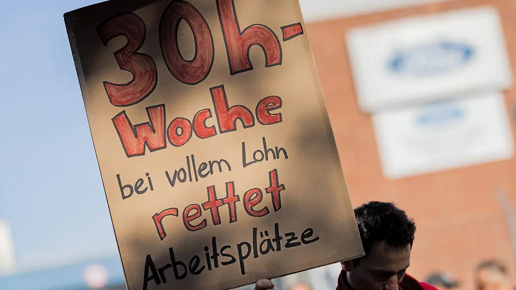 Ein-Mitarbeiter-haelt-ein-Plakat-mit-der-Aufschrift-30h-Woche-bei-vollem-Lohn-rettet-Arbeitsplaetze-beim-ersten-Streik-der-Geschichte-vor-den-Koelner-Ford-Werken-Bei-den-Koelner-Ford-Werken-kommt-es-erstmals-zu-einem-Streik-Die-Protestaktion-gegen-einen-geplanten-Stellenabbau-an-dem-Standort-mit-11-500-Beschaeftigten-soll-am-Mittwochmorgen-beginnen-und-bis-zum-Ende-der-Nachtschicht-am-Donnerstagmorgen-dauern-wie-die-IG-Metall-mitteilte