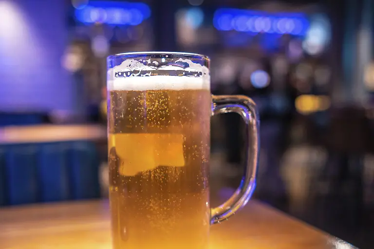 Kaltes-Bier-auf-dem-Tisch-in-einem-lebhaften-Londoner-Pub-das-Freunde-zu-einem-erfrischenden-Getraenk-in-einer-lebhaften-Abendatmosphaere-einlaedt-Modellfreigabe-vorhanden