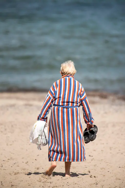 Eine-Frau-im-Bademantel-geht-zum-Bad-in-die-Ostsee-am-Ostseestrand-von-Warnemuende-Derzeit-ist-das-Urlaubswetter-an-Mecklenburg-Vorpommerns-Ostseekueste-durchwachsen