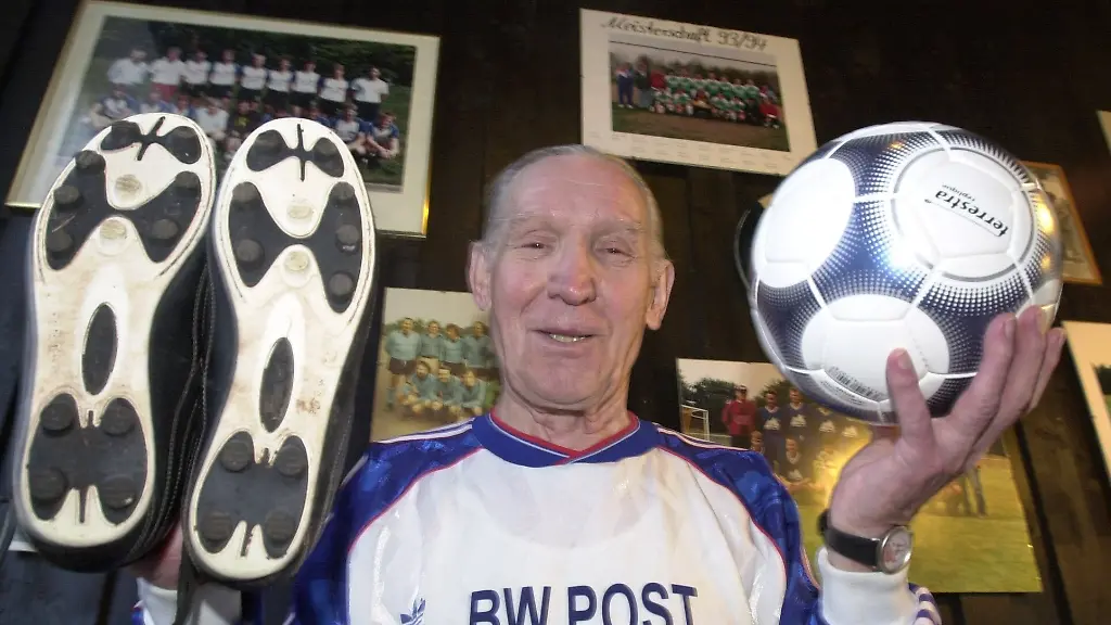 Mit-Fussballschuhen-und-ball-posiert-Fussball-Opa-Kurt-Meyer-am-09-01-2002-in-seinem-Trikot-vor-alten-Bildern-im-Vereinsheim-des-Provinzclubs-Blau-Weiss-Post-Recklinghausen-Der-vermutlich-aelteste-aktive-Fussballspieler-Deutschlands-wird-am-13-01-2002-in-der-ARD-Sportschau-als-Torschuetze-des-Jahres-ausgezeichnet-nachdem-er-vor-gut-einem-Jahr-bei-einem-Spiel-anlaesslich-seines-80-Geburtstags-aus-16-Meter-ein-Tor-gegen-den-FC-Hillerheide-erzielte-und-zum-Torschuetzen-des-Monats-Januar-gewaehlt-wurde-Derzeit-muss-Meyer-wegen-einer-Erkaeltung-eine-Fussballpause-einlegen